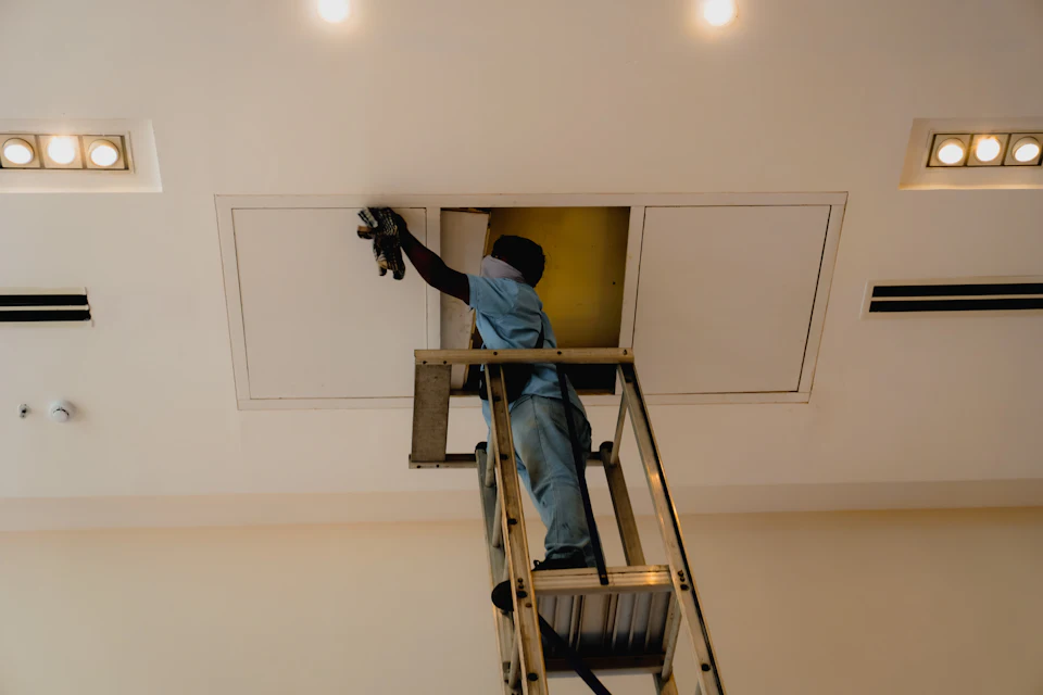 Electrician on a ladder working above a commercial ceiling